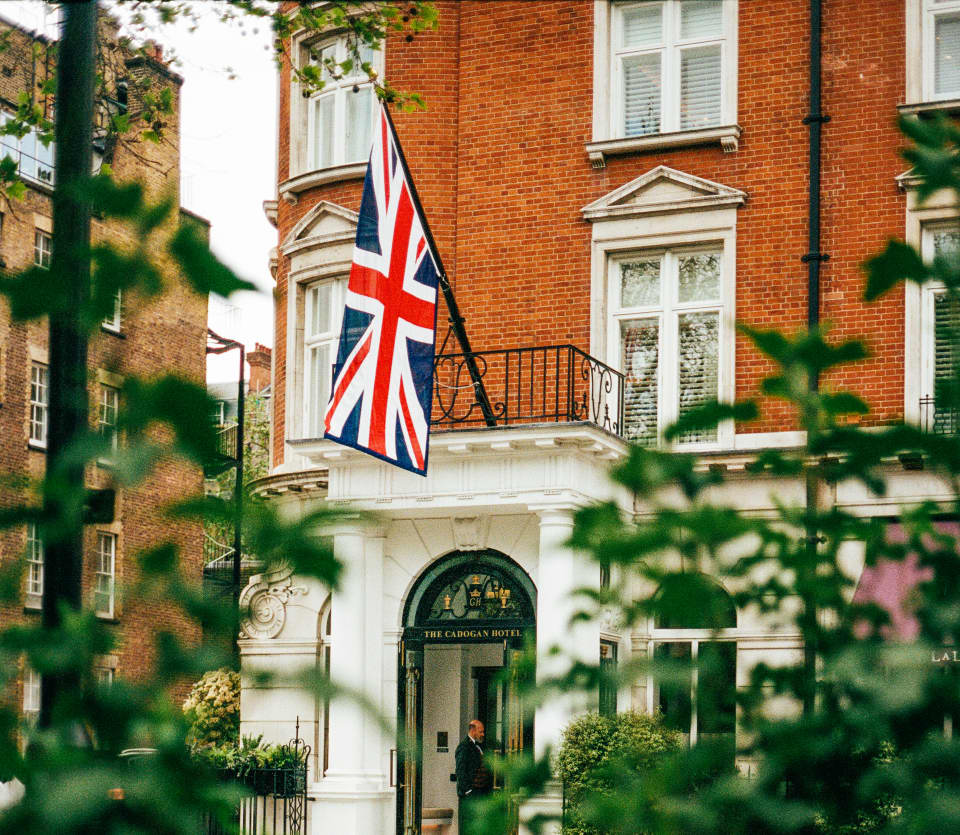 View from Cadogan Place Garden across foliage and over railings to the hotel's white portico entrance, with Union Jack above.