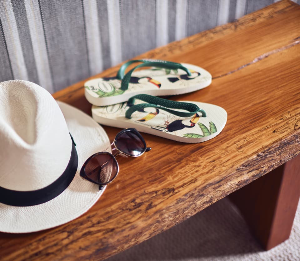 White Panama hat with sunglasses and flip flops on a wooden bench