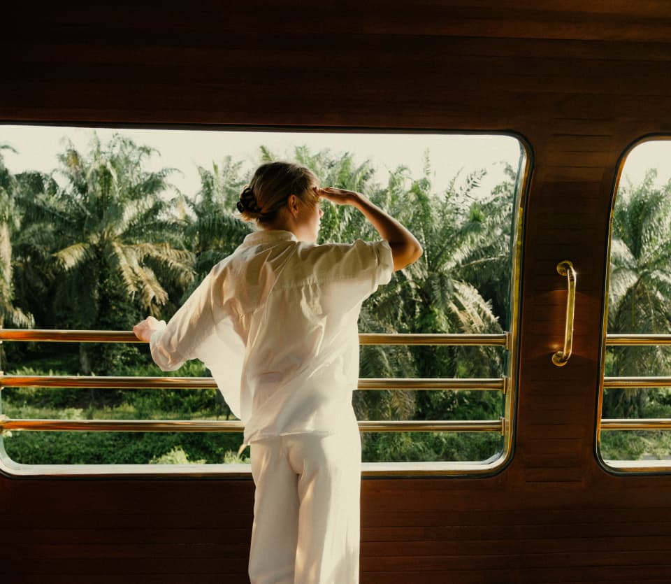 A woman in translucent white top and trousers shields her eyes as she gazes at the view from the Observation Deck rails.