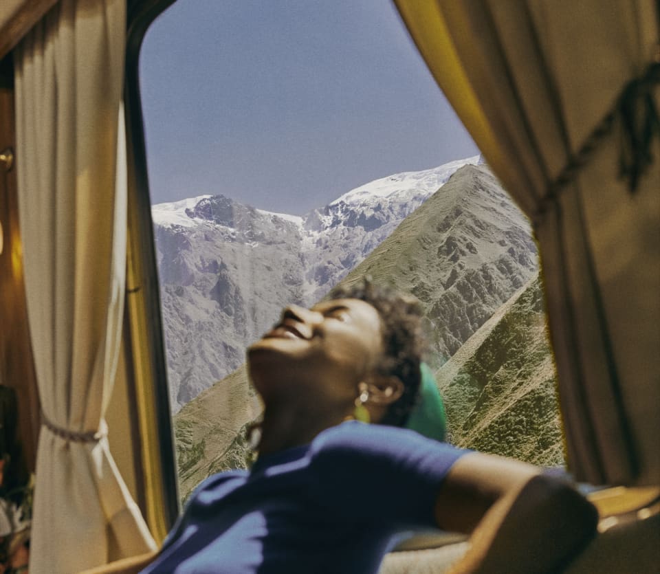 A female guest in a blue top basks in sunshine from the window behind her, which has views onto the incredible Andean peaks.
