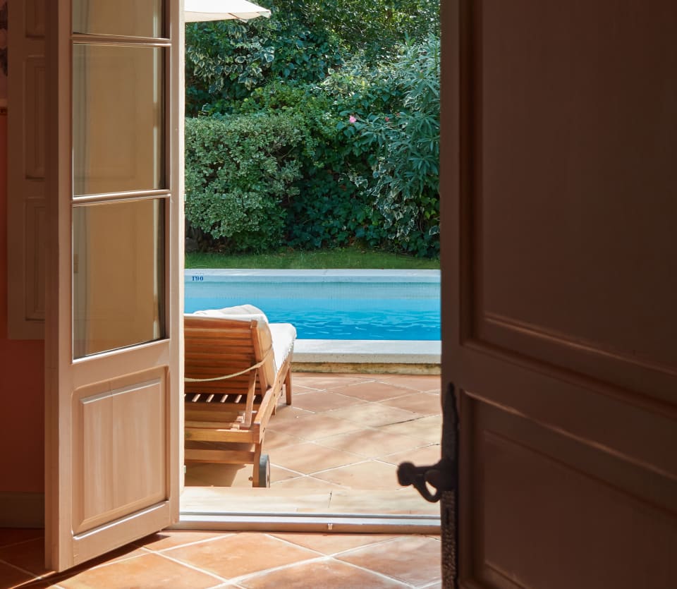 Warm terracotta surrounds the shimmering pool, set in lush gardens, seen through an open door of the Matthew Williamson Suite.