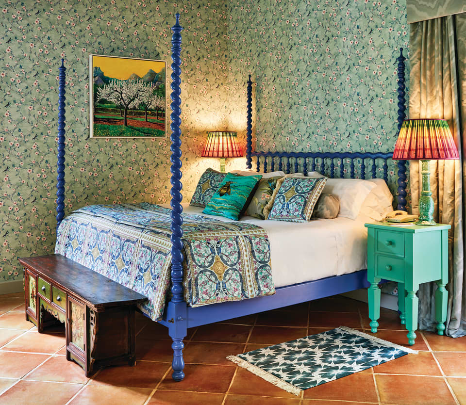 Indigo blue four-poster king-bed in a hotel room with vibrant floral wallpaper