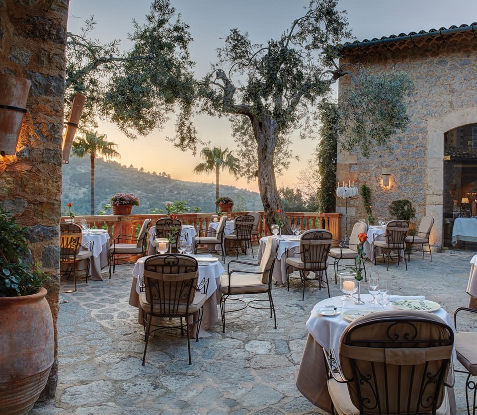 Stone-tiled restaurant patio dotted with formal candlelit tables at sunset