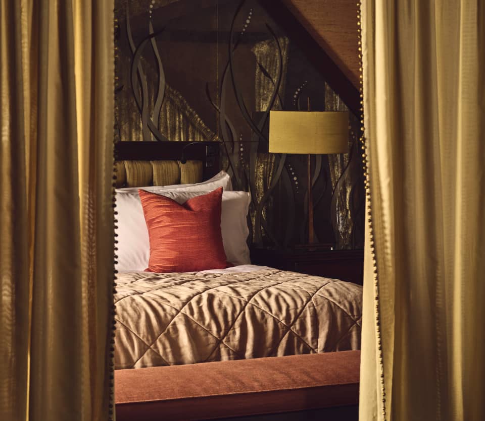 Parted gold drapes reveal a bed with a russet silk cushion, peach quilt and pink pillows in the Jade 'Les Jardins' Suite.