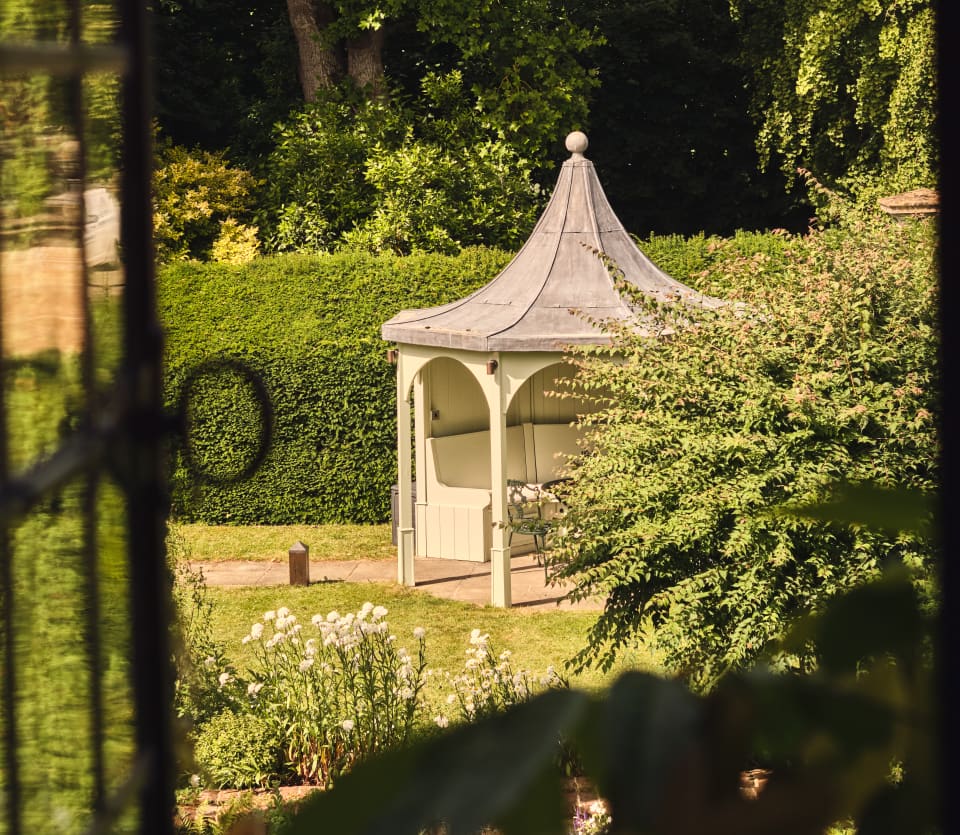 View from an open upper window of an Oxborough gazebo below, which provides shaded seating in the sunny green gardens.