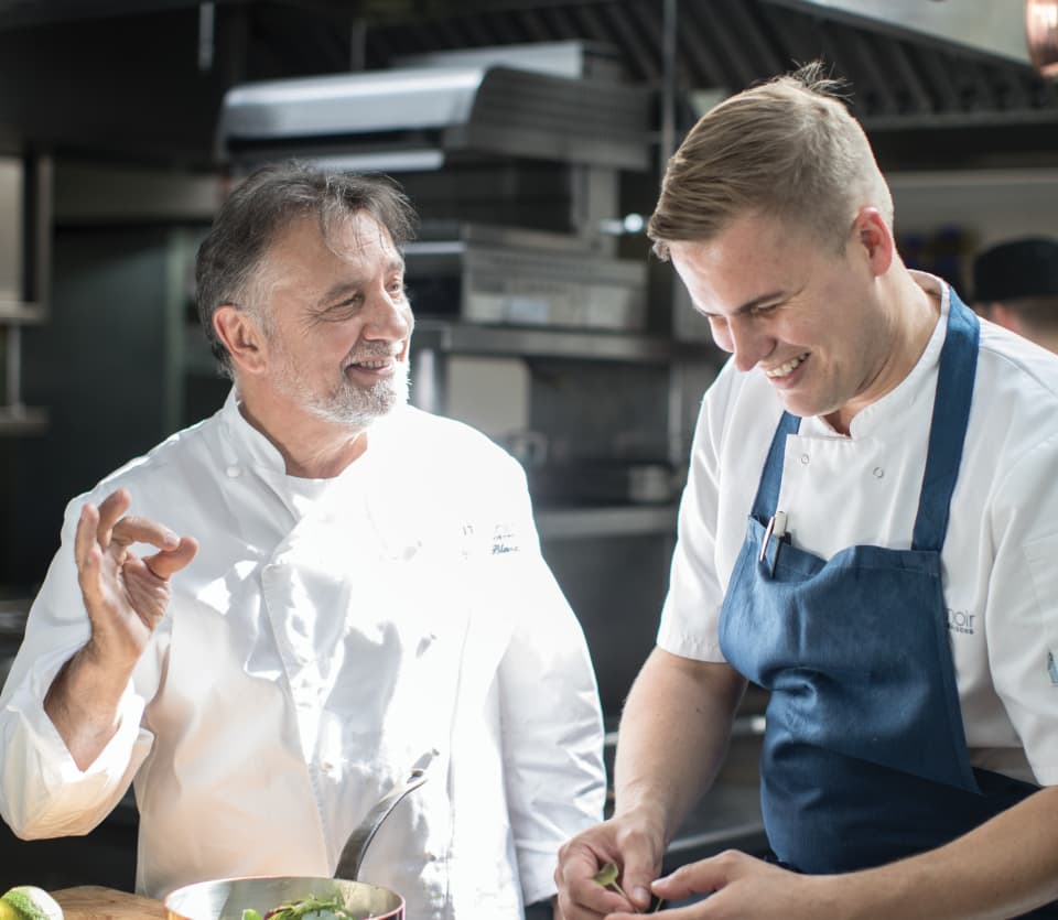 Raymond Blanc smiling as he discusses a recipe with another smiling chef