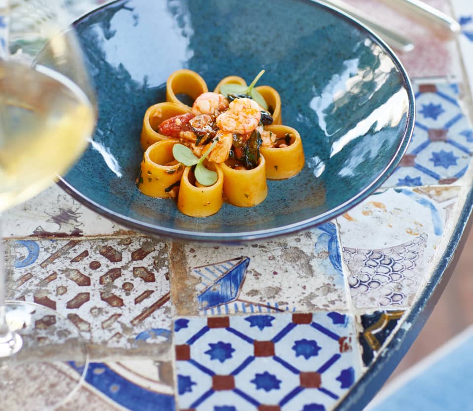 Close-up of a teal blue ceramic bowl containing a pasta dish in a petal formation